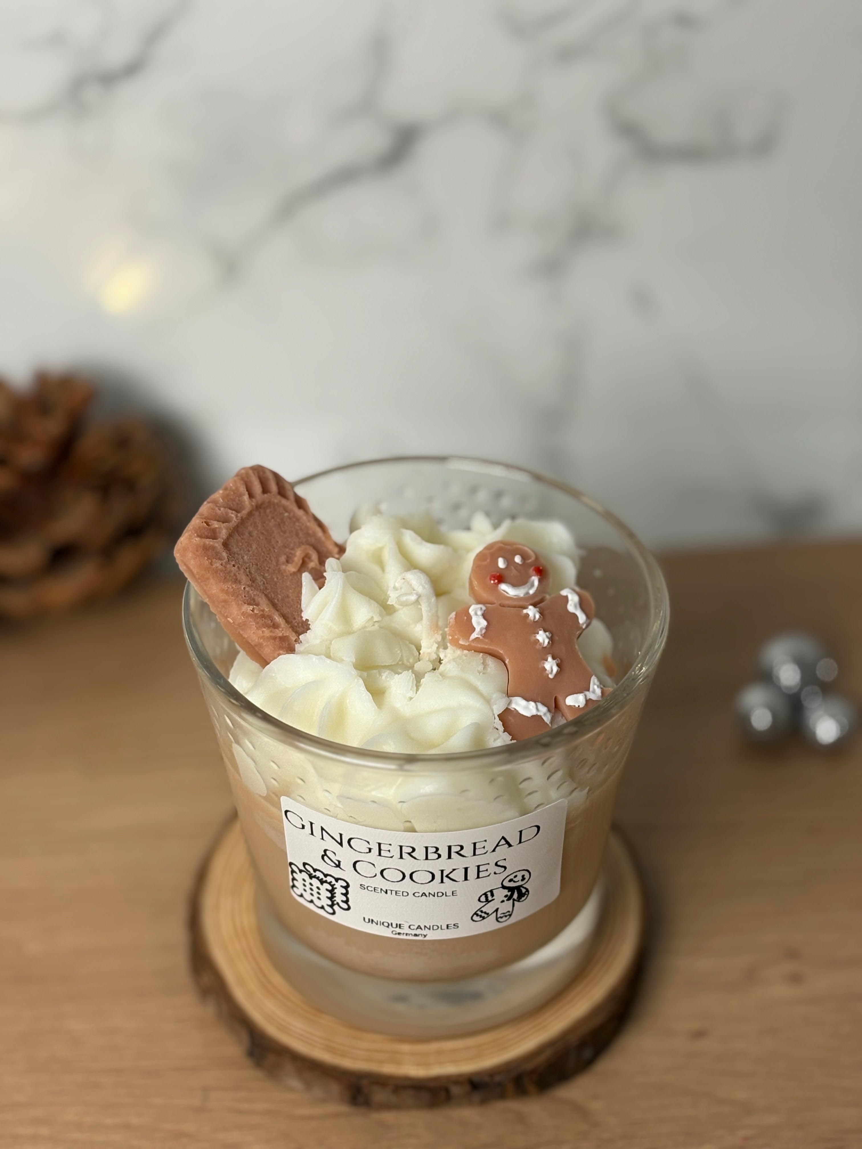 Handgegossene Bio-Sojawachs Duftkerze "Gingerbread & Cookies" im Glas auf einem Holzuntersetzer. Die Kerze hat eine cremige Wachs-Sahnehaube, dekoriert mit einem kleinen Spekulatius-Keks und einem Lebkuchenmann aus Wachs. Perfekte Weihnachtsdeko mit Spekulatiusduft.