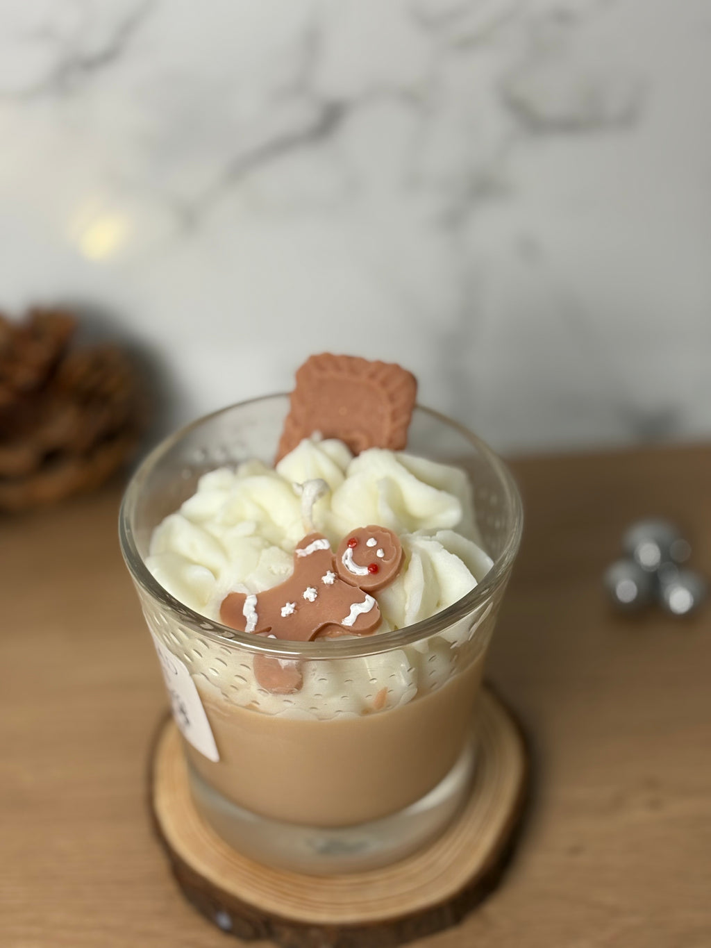 Handgegossene Bio-Sojawachs Duftkerze "Gingerbread & Cookies" im Glas auf einem Holzuntersetzer. Die Kerze hat eine cremige Wachs-Sahnehaube, dekoriert mit einem kleinen Spekulatius-Keks und einem Lebkuchenmann aus Wachs. Perfekte Weihnachtsdeko mit Spekulatiusduft.