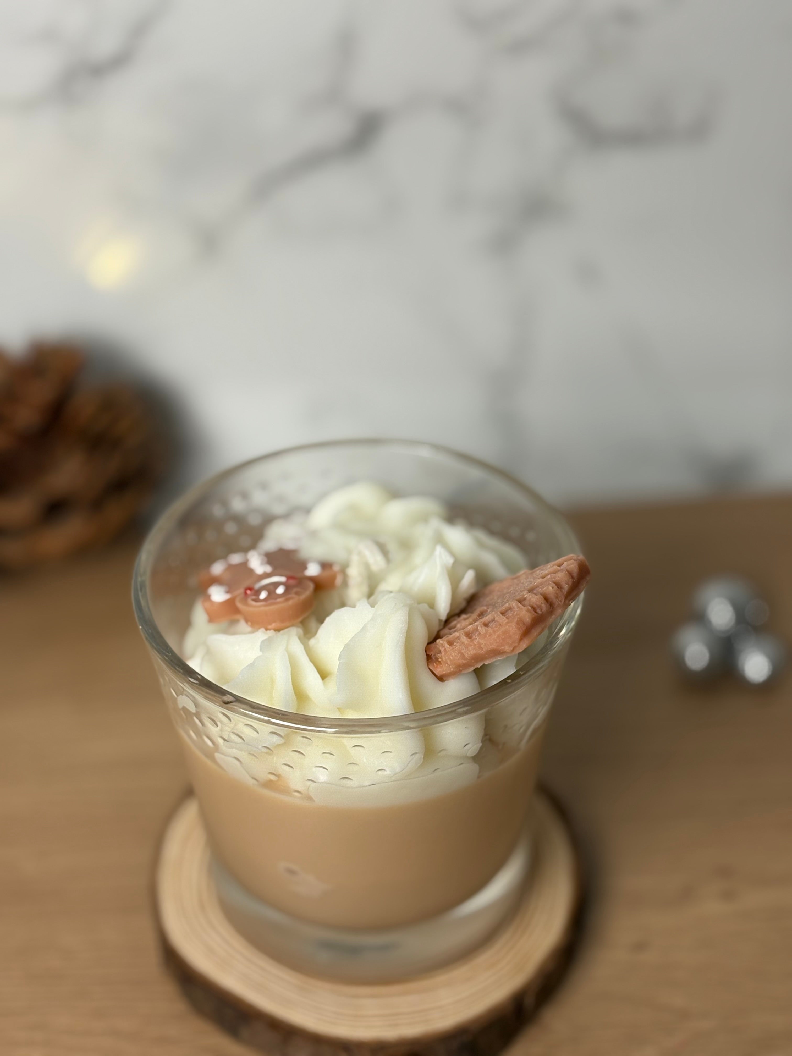 Handgegossene Bio-Sojawachs Duftkerze "Gingerbread & Cookies" im Glas auf einem Holzuntersetzer. Die Kerze hat eine cremige Wachs-Sahnehaube, dekoriert mit einem kleinen Spekulatius-Keks und einem Lebkuchenmann aus Wachs. Perfekte Weihnachtsdeko mit Spekulatiusduft.